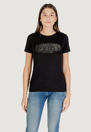 T-shirt di cotone nero con logo "GUESS" glitterato al centro, maniche corte e collo rotondo, abbinato a jeans azzurri chiari.