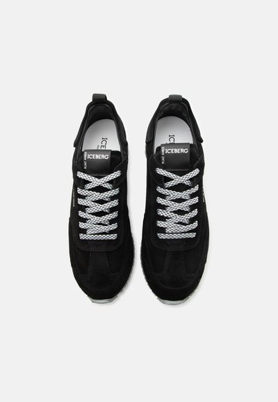 Μαύρα δερμάτινα αθλητικά παπούτσια με λευκά κορδόνια με σχέδια, ετικέτα "ICEBERG από το 1974" στα γλώσσες, από πάνω σε λευκό φόντο.