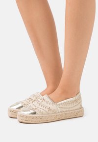 Espadrilles beige con punte metalliche argento, motivi floreali ricamati, suole in corda di juta e design slip-on.