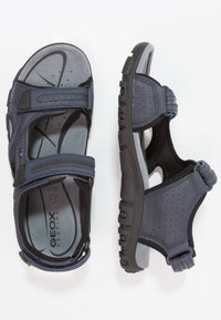 Tume sinised sandaalid võrkmaterjalist pealsega, Velcro rihmadega, pehmendustega sisetallad ja vastupidav must kummi tald, millel on drenaažiaugud.
