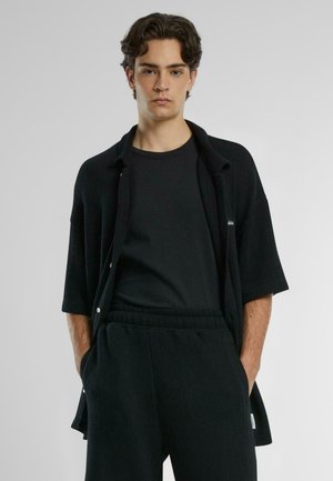 Black ribbed knit shirt with short sleeves, layered over a black crewneck t-shirt, paired with matching ribbed black pants.