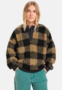 Fleece pullover in zwart en bruin geruit patroon, met een zwarte drukknoopsluiting en ribgebreide manchetten, met een gestructureerde, zachte afwerking.