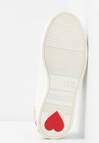 Vit sneakersula med röd hjärtdekoration. Texten "LOVE MOSCHINO" präglad. Texturerad yta med horisontella ränder. Gummimaterial.