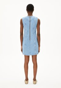 Mouwloze denim jurk in lichtblauw met een ritssluiting aan de achterkant. Heeft een getailleerde silhouette en een zachte denim textuur.
