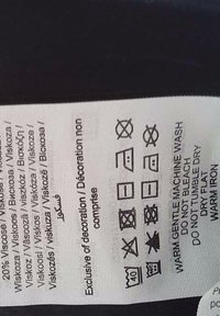 Étiquette de vêtement indiquant 20 % de viscose et des symboles d'entretien incluant lavage en machine doux et chaud, pas d'eau de javel, ne pas utiliser de sèche-linge, sécher à plat, repasser à chaud.