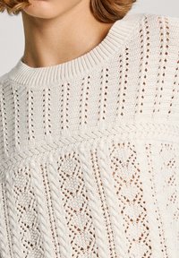 Weißer Strickpullover mit strukturiertem Muster, offenen Maschen und Zopfmustern, rundem Ausschnitt und geripptem Saum.