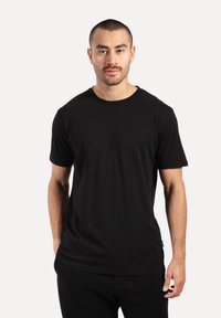 Camiseta negra de manga corta hecha de algodón. Cuello redondo, ajuste relajado y textura suave. Lleva puesta una persona sobre un fondo liso.