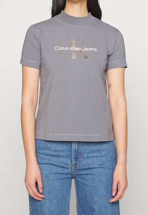 Grey cotton t-shirt with a high neckline and short sleeves. Features a white and gold Calvin Klein Jeans logo printed on the front.