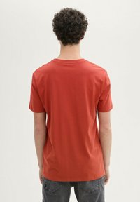 Rød bomulds T-shirt med korte ærmer og rund hals. Glat tekstur med en afslappet pasform og lige kant, båret med mørkegrå bukser.