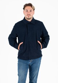 Giacca di velluto a coste blu navy con colletto, tasche frontali e design a taglio dritto. Indossata sopra jeans azzurri chiari.