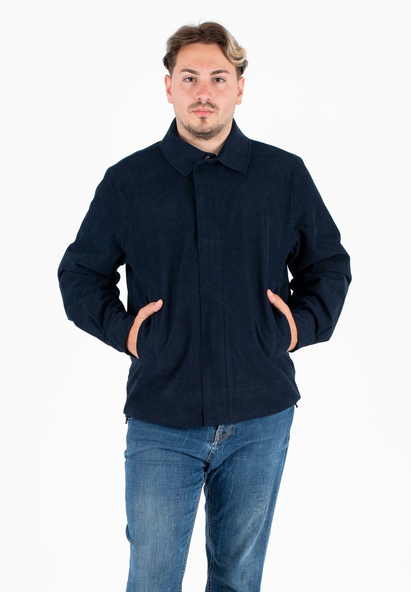 Marineblauwe corduroy jas met een kraag, voorzakken en een rechte snit. Draagt over lichtblauwe jeans.