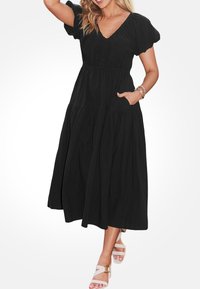 Czarna midi sukienka z dekoltem w kształcie v, bufiastymi rękawami, elastycznym pasem i warstwową spódnicą. Posiada boczne kieszenie i gładką fakturę.