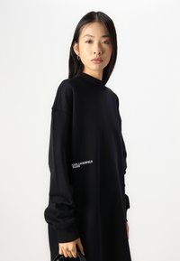 Hanorac negru supradimensionat cu guler înalt și umeri căzuți. Prezintă logo-ul alb "KARL LAGERFELD JEANS" pe partea stângă. Textură moale.