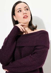 Pull purple lavorato a maglia con design off-the-shoulder. Texture a coste, maniche lunghe e ampia scollatura. Aspetto complessivo liscio.