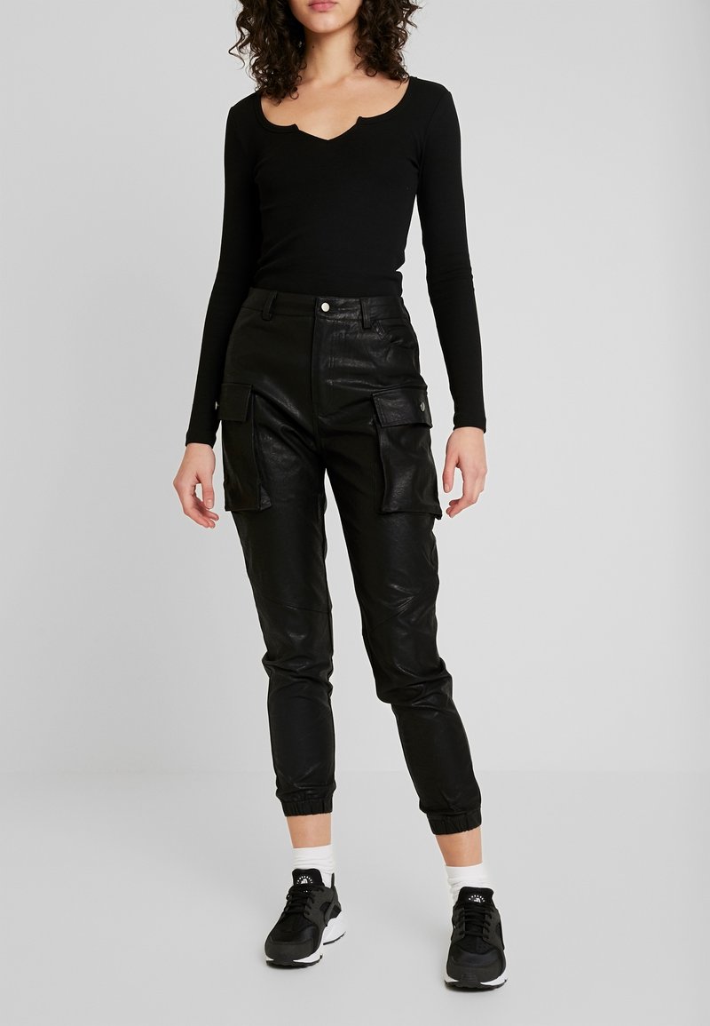 Černý dlouhý rukáv s výstřihem do U, zkombinovaný s černými vysokými cargo kalhotami z umělé kůže, které mají boční kapsy a elastický manžet.