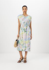 Blomstermønstret, pastellfarget kjole med korte ermer, elastisk midje og lengde til midt på leggen. Brukt med svarte sandaler med stropper og en flettet veske.