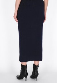 Fustă midi tricotată în dungi de un navy, cu un design ajustat, de culoare uniformă și o textură netedă. Asortată cu cizme cu toc înalt, negre.
