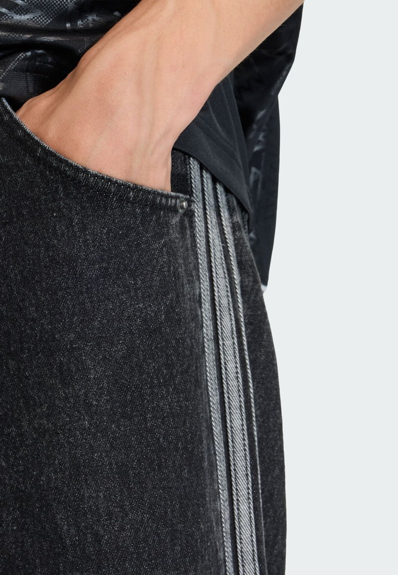 Schwarze Jeanshose mit distressed Textur, ausgestattet mit einer Seitentasche und grauen vertikalen Streifen entlang der Nähte.