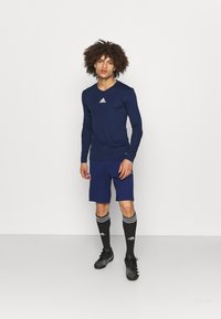 Adidas navy langærmet skjorte, matchende shorts, sorte knæstrømper med hvide striber og sorte fodboldsko med prikkede detaljer.