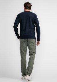 Navy long-sleeve shirt with a crew neck, paired with olive green pants. Model wears white sneakers, standing against a plain backdrop.