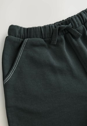Pantalones de chándal de color verde oscuro con un cinturón elástico, cordones, bolsillos laterales y detalles de costura blanca en contraste. Textura suave y acanalada.