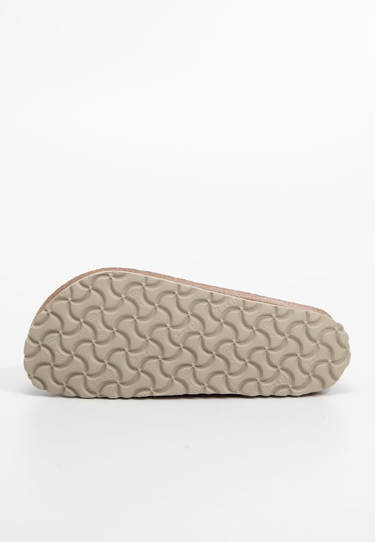 Semelle de sandale en caoutchouc beige texturé avec un motif ondulé entrelacé, présentée sur un fond blanc.