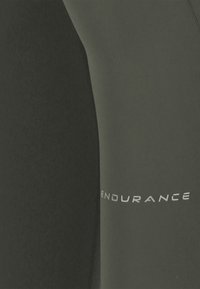 Close-up af sort og mørkegråt stof med "ENDURANCE" trykt i hvidt på sømmen mellem de to farver.