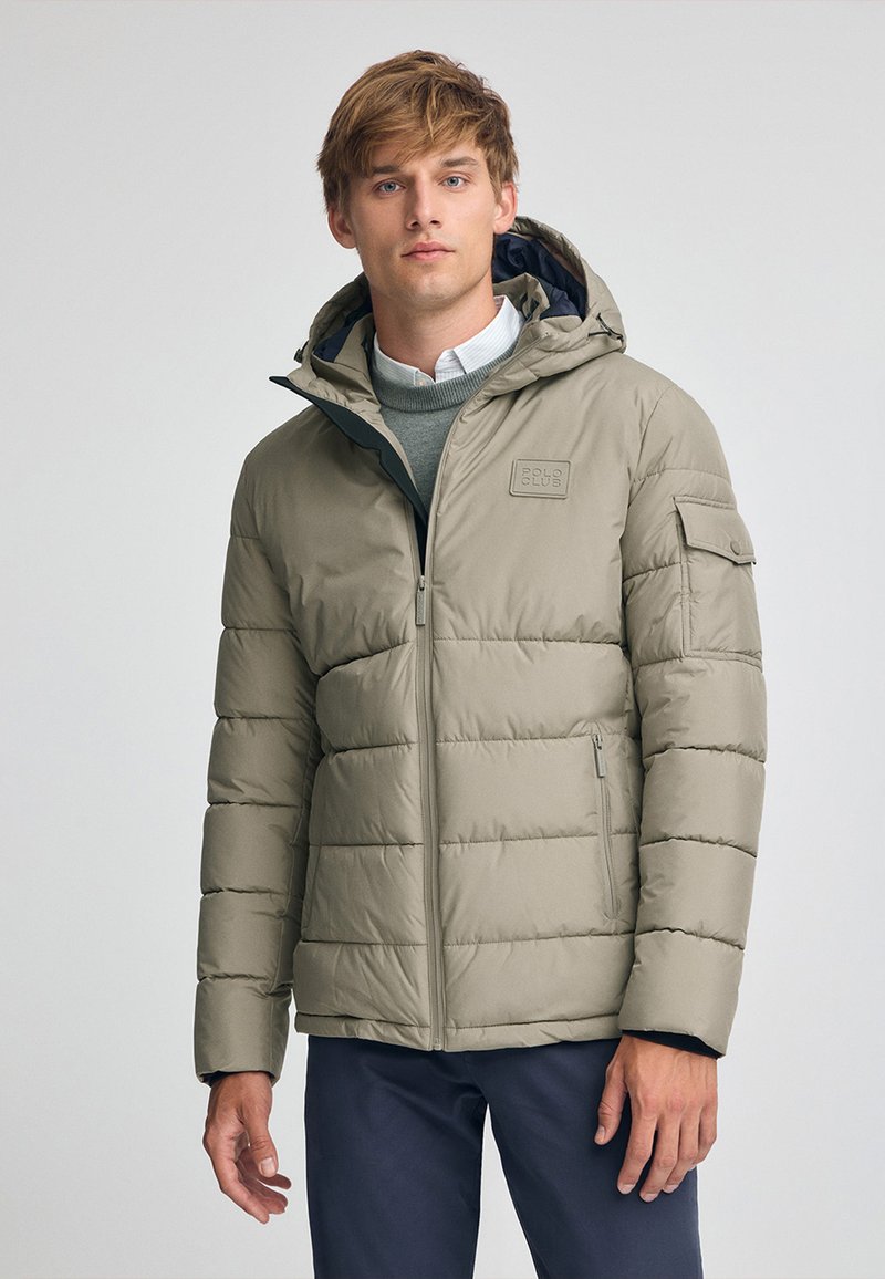 Giacca puffer beige chiaro con texture a trapunta orizzontale, cappuccio, zip frontale e tasche laterali. Presenta una patch con logo sul petto e un rivestimento interno a contrasto.