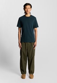 Teal bomulds t-shirt med rund hals, parret med olivengrønne cargo bukser med flere lommer, båret med beige slip-ons.