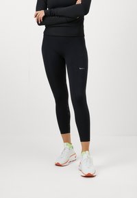 Sorte atletiske leggings med slim fit, der har reflekterende detaljer på siden, kombineret med hvide sneakers og en sort langærmet bluse.