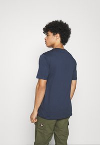 T-shirt de algodão azul-escuro com mangas curtas, decote redondo e um corte descontraído, combinada com calças cargo verde-azeitona. Design simples, sem padrões.