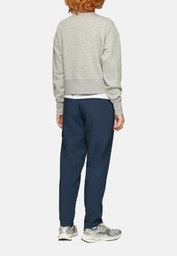 Grijze cropped sweatshirt met doorgezakte schouders, marineblauwe joggingbroek en grijze hardloopschoenen met metallic accenten, gezien van achteren.