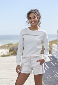 Cream sweatshirt with a horizontal multicolored stripe, paired with matching cream shorts featuring side stripe accents. Cotton blend material.