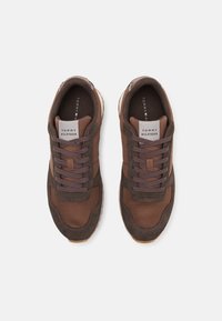 Sneaker atletiche marroni con tomaia in suede e mesh, dotate di una suola spessa marrone, chiusura con lacci e dettagli con logo sulla linguetta.