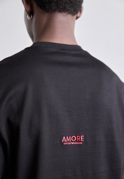 T-shirt en coton noir avec le texte brodé rouge « AMORE » et « EMPORIO ARMANI » au dos. Texture douce et design classique à col rond.
