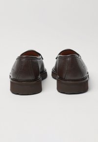 Ciemnobrązowe skórzane buty o teksturowanym wykończeniu, zaokrąglonym nosku, przeszyciach ozdobnych i gumowej podeszwie. Widok od tyłu.