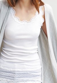 Top bianco a costine con scollo in pizzo a zig zag e orlo in pizzo a strati. Abbinato a un cardigan grigio chiaro.