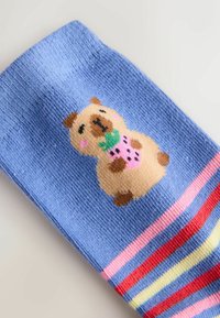 Niebieska skarpetka z kreskówkowym misiem trzymającym truskawkę i wielokolorowymi paskami w pobliżu ściągacza.