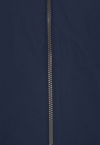 Marineblauwe stoffen jas met een centrale rits, gladde textuur, duurzaam materiaal en contrasterende metalen ritshardware.