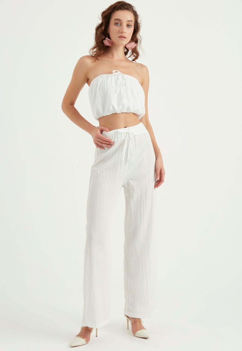 Vit tvådelad outfit bestående av en axelbandslös crop top och vida byxor, i textil med en elastisk midja.