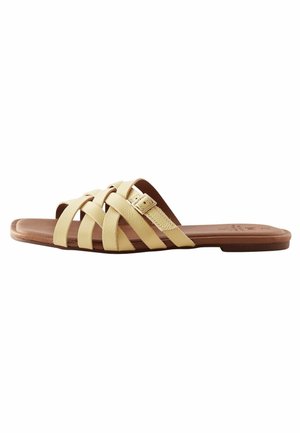 Gelbe Leder-Sandale mit mehreren übereinander kreuzenden Riemen, flacher brauner Sohle und einem Schnallenakzent für eine verstellbare Passform.