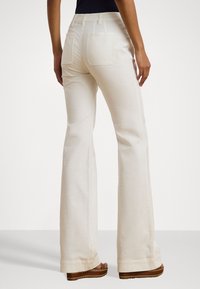 Witte uitlopende broeken van zachte, gestructureerde stof, met achterzakken en een hoge taille, gecombineerd met bruine plateau schoenen.