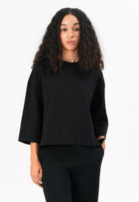 Schwarzer strukturierter Pullover mit einer leicht oversize Passform, langen Ärmeln und rundem Halsausschnitt, kombiniert mit passenden enganliegenden Hosen.