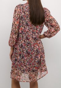 Květinové šaty s černým pozadím, zdobené růžovými, oranžovými a fialovými květy, dlouhými nafouklými rukávy a volným střihem. Průhledná látka.