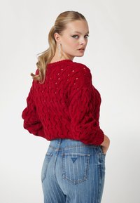 Pull rouge en tricot avec un motif en cable, coupé ample et manches longues. Porté avec un jean taille haute à rayures bleues avec un détail de logo.