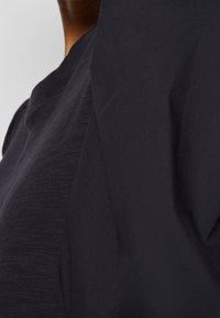 Dark navy t-shirt with a textured fabric. Close-up view reveals a round neckline and slight draping detail on the sleeves and body.