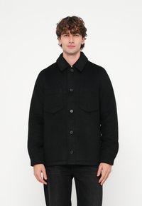 Sort uldblandet jakke med knaplukning foran, store påsyede lommer og en spids krave. Har en tekstureret finish og en afslappet pasform.