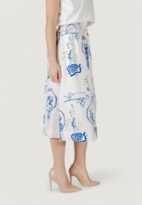 Una gonna bianca, al ginocchio, con motivi floreali blu, caratterizzata da un cinturino arricciato e una texture liscia. Abbinata a tacchi alti nudi.