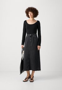 Bodysuit negro de manga larga combinado con una falda de mezclilla negra de tiro alto, que presenta un dobladillo deshilachado y un cierre frontal de botones, complementado con sandalias negras.