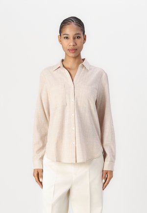 Beige skjorte med knapper og tekstur, lange ermer og to brystlommer, kombinert med lysfargede vide bukser.
